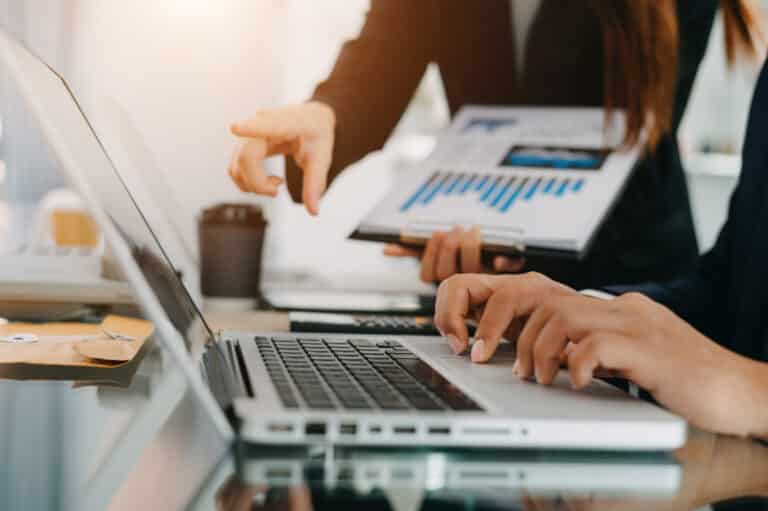 Business documents on office table with smart phone and calculator digital tablet and graph business with social network diagram and two colleagues discussing data working in the office