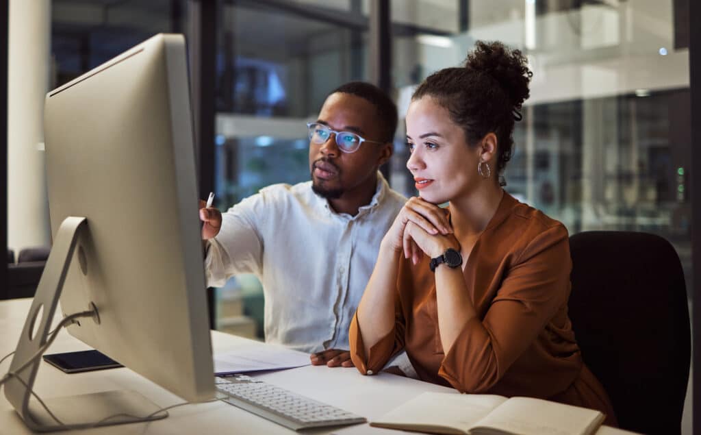 Business training, night planning and employees talking about corporate proposal on internet in dark office at night. African workers working on partnership on the web with computer during overtime.